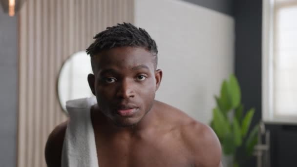 Africký Američan péče o obličej oholené vousy hydratační pleť při pohledu na kameru mužské krásy ranní hygieny v domácnosti koupelna mladý hipster chlap použití hydratační krém po holení péče - Záběry, video
