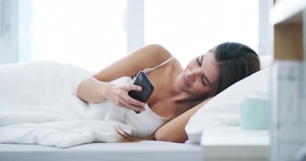 Smile, woman and phone in bedroom for typing, reading social media notification or scroll mobile app in the morning at home. Smartphone, relax or wake up in bed to search internet, contact or network. - Footage, Video