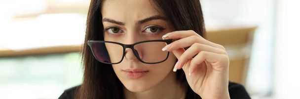 Gestionnaire féminin sérieux enlève les lunettes regardant dans la caméra. Une jeune femme avec une expression faciale suspecte est assise au bureau - Photo, image