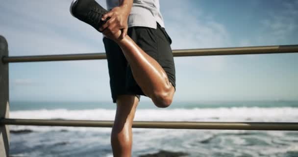 Oceaan, man en benen strekken voor training op de promenade in Kaapstad voor fitness aan het strand. Atleet, hardloper en sportief met de hand op de voet voor stijve spieren met lichaamsbeweging voor cardio, gezondheid of wellness. - Video