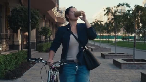 Kaukasische Frau trinkt morgens Kaffee, während sie vor der Arbeit Fahrrad fährt. Eine Geschäftsfrau fährt mit dem Fahrrad ins Büro. Hochwertiges 4k Filmmaterial - Filmmaterial, Video