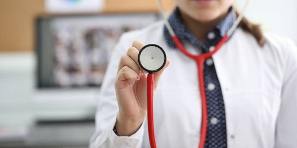 Close-up view of faceless medical female worker in uniform showing part of red stethoscope on camera. Planned check-up and diagnostics at clinic concept - Photo, Image