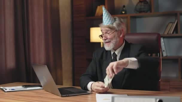 Grey-haired male in glasses wearing suit and birthday hat throwing paper money in air while looking at laptop screen. Upset older employee dealing with financial failure in business project at work. - Footage, Video