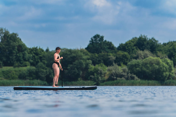 attractive woman in swimwear on supboard in the middle of the lake - Photo, Image