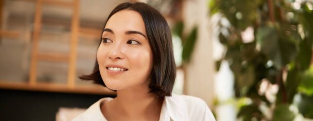 Detailní portrét krásné, romantické mladé asijské ženy, usmívající se a vypadající šťastně, sedí v útulné kavárně. Kopírovat prostor - Fotografie, Obrázek