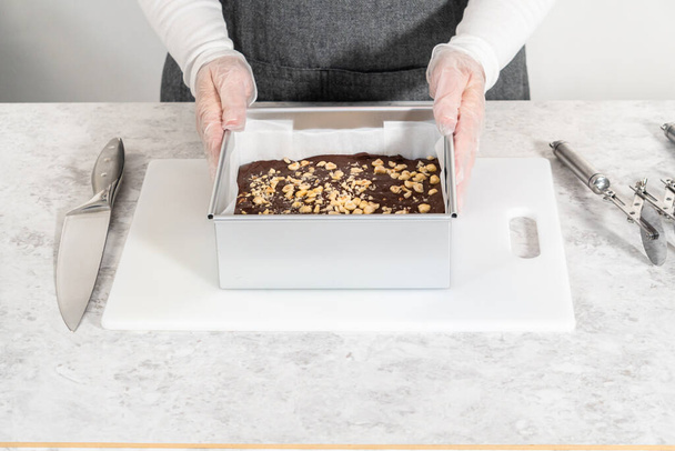 Rimuovere il cioccolato fondente di nocciole da una teglia quadrata rivestita con pergamena. - Foto, immagini