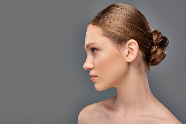 side view of young woman with perfect skin and bare shoulders looking away on grey background - Photo, Image