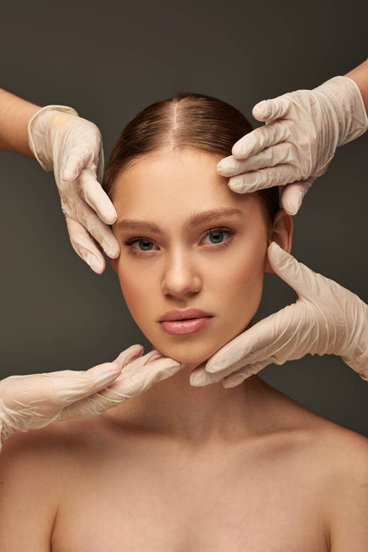 estetiste in guanti medici esaminando volto di giovane donna su sfondo grigio, concetto di dermatologia - Foto, immagini
