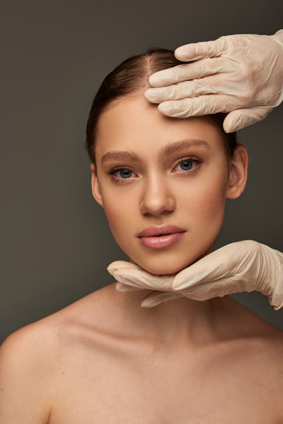 esteticista em luvas médicas tocando rosto de mulher jovem em fundo cinza, dermatologia conceito - Foto, Imagem