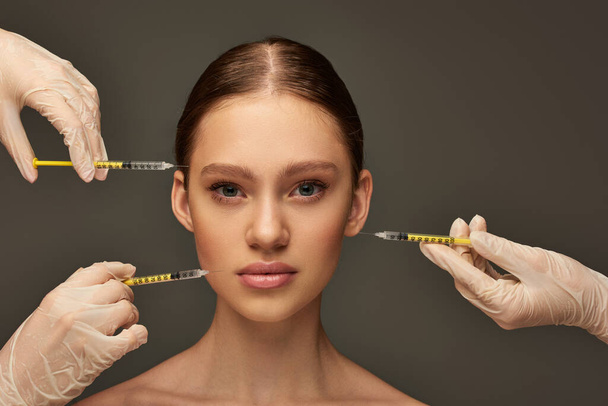 esteticistas em luvas médicas segurando seringas perto de mulher jovem em fundo cinza, procedimento - Foto, Imagem