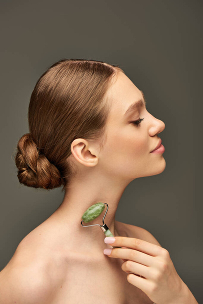 young woman with closed eyes doing neck massage with jade roller on grey background, rejuvenation - Photo, Image