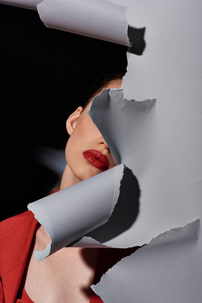 vista parcial de mujer joven con labios rojos posando cerca de papel gris roto, maquillaje audaz y moda - Foto, Imagen