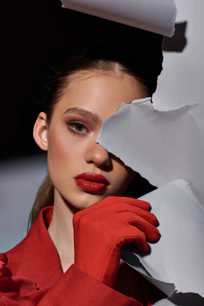 attraente giovane donna con labbra rosso brillante posa vicino strappato carta grigia e guardando la fotocamera - Foto, immagini