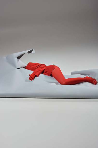 femme recadrée en tenue rouge avec des gants et des collants couchés près du papier déchiré sur fond gris - Photo, image