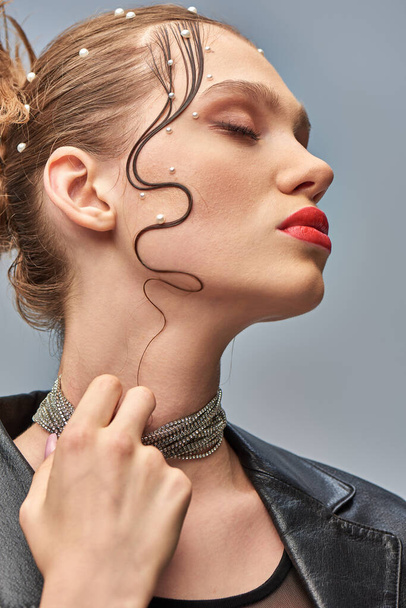 retrato de jovem glamourosa com alfinetes de pérola no cabelo tocando colar no fundo cinza - Foto, Imagem