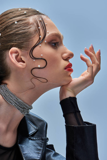 Seitenansicht des hübschen jungen Models mit trendigen Perlstiften im Haar und roten Lippen, die vor grauem Hintergrund posieren - Foto, Bild