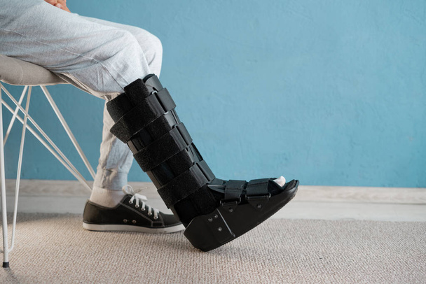 Hombre lesionado con ortesis y esguince de tobillo sentado en la silla. Concepto de ortesis de tobillo. Copiar espacio - Foto, imagen