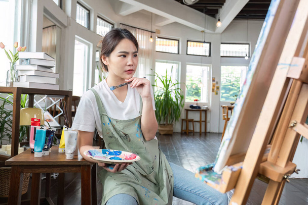 Закрыть картину счастливой молодой азиатки, рисующей кисть на холсте в студии живописи. В классе художественной мастерской.. - Фото, изображение