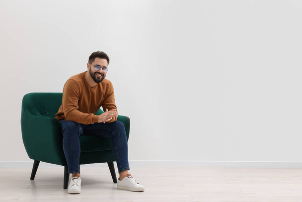 Handsome man sitting in armchair near white wall indoors, space for text - Photo, image