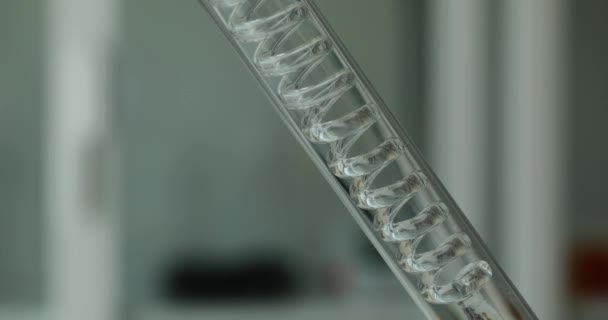 Vista de primer plano del líquido transparente que fluye lentamente a través del tubo espiral dentro del tubo de ensayo. Líquido purificador en laboratorio - Imágenes, Vídeo