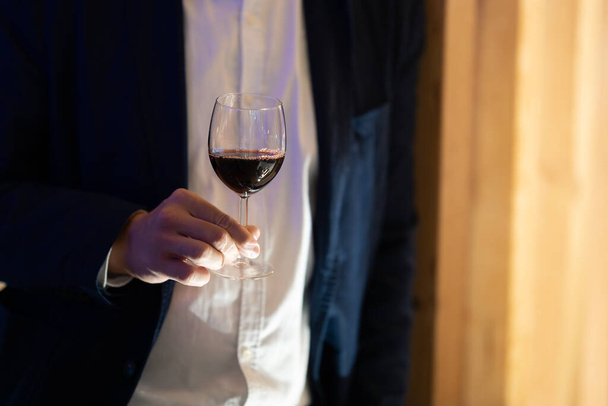 Een hand die subtiel een wijnglas vastgrijpt, een moment van verwennerij vangt. - Foto, afbeelding