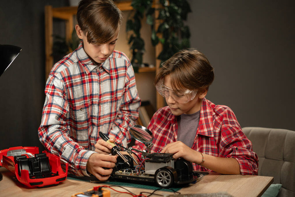 Teini-ikäiset veljet opiskelevat elektroniikkaa tehden autoa huoneensa kaukosäätimellä, työskennellen tiedeprojektissa. Kopioi tila - Valokuva, kuva