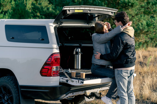 Młoda para zakochana chłopak i dziewczyna odpoczywają razem w bagażniku samochodu przytulając się i całując na zewnątrz na polu - Zdjęcie, obraz