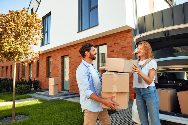 A young married couple unloads boxes of things from a car and carries them to a new home. Renting and buying a home. Moving concept. - Photo, Image