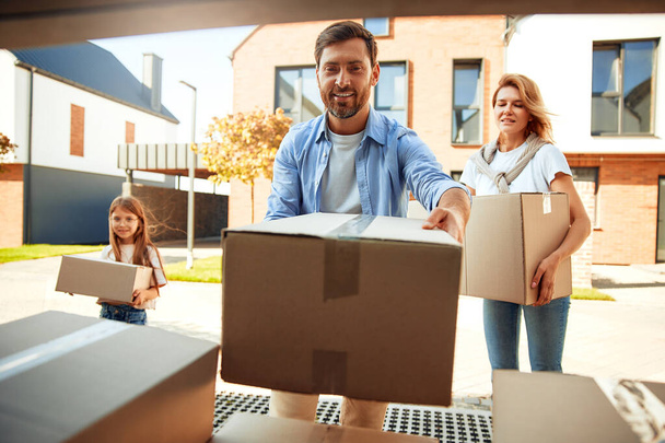 A young married couple with their daughter unloads boxes of things from a car and carries them to a new home. Renting and buying a home. Moving concept. - Photo, Image
