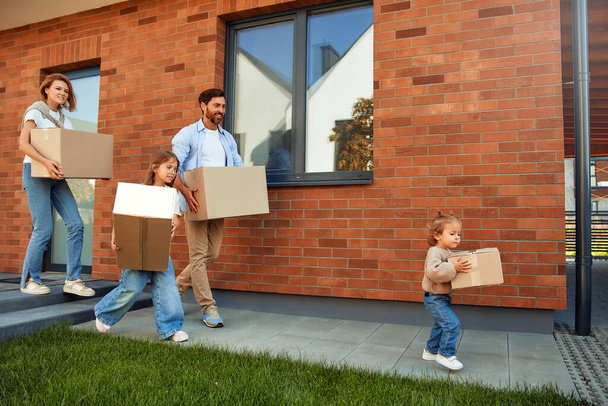 Una familia joven con dos hijas hijos lleva cajas de cosas en el coche. Alquilar y comprar una casa. Mudarse a un nuevo hogar. - Foto, Imagen