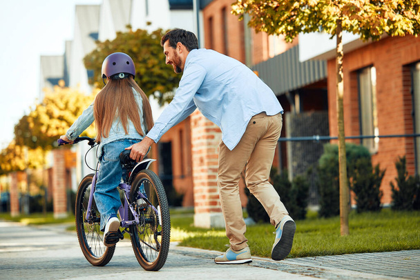 Un padre felice ha insegnato alla sua figlioletta ad andare in bicicletta. Un bambino impara ad andare in bicicletta. Attività per famiglie in estate. - Foto, immagini