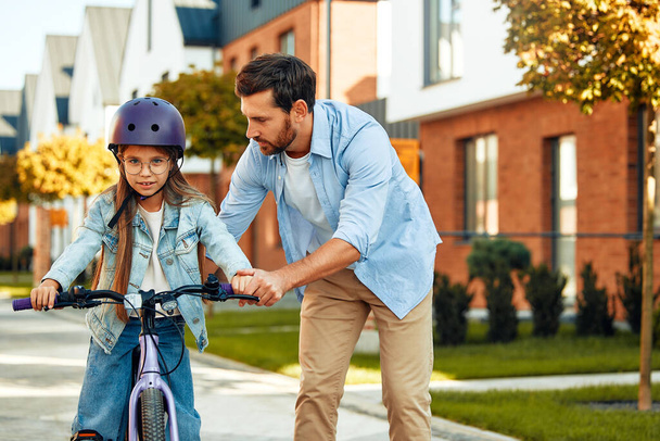 Ein glücklicher Vater brachte seiner kleinen Tochter das Fahrradfahren bei. Ein Kind lernt Fahrradfahren. Familienaktivitäten im Sommer. - Foto, Bild