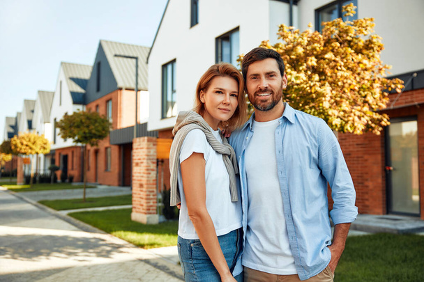 Una giovane coppia di sposi felici in piedi vicino a una nuova casa e abbracciati. Affittare e comprare una casa. Concetto in movimento. - Foto, immagini