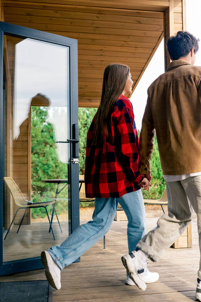Jovem e garota apaixonados de mãos dadas saem no terraço de uma casa de madeira para passear na natureza - Foto, Imagem