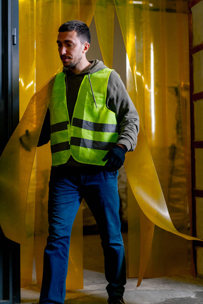 Egy munkaruhát viselő hulladék-újrafeldolgozó állomás alkalmazottja átsétál egy szilikon függönyön az üzem ajtajában. - Fotó, kép