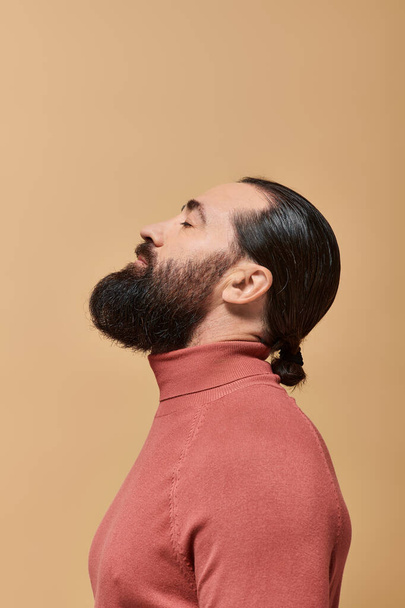 oldal kilátás jóképű férfi szakáll pózol rózsaszín garbó jumper bézs háttér - Fotó, kép
