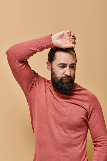 portrait, handsome man with beard posing in pink turtleneck jumper on beige background, serious face - Photo, Image