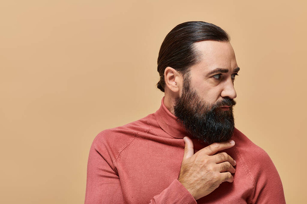 portrét pohledného muže s vousy pózujícího v roláku svetr na béžovém pozadí, vážná - Fotografie, Obrázek