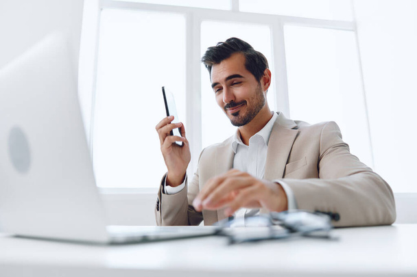 Człowiek w biurze biznesmen siedzi przy biurku i pracuje w laptopie i rozmawia przez telefon, nowoczesny garnitur, finanse i startup koncepcja i analiza danych, styl życia pracy w jasnym biurze. Wysokiej jakości zdjęcie - Zdjęcie, obraz