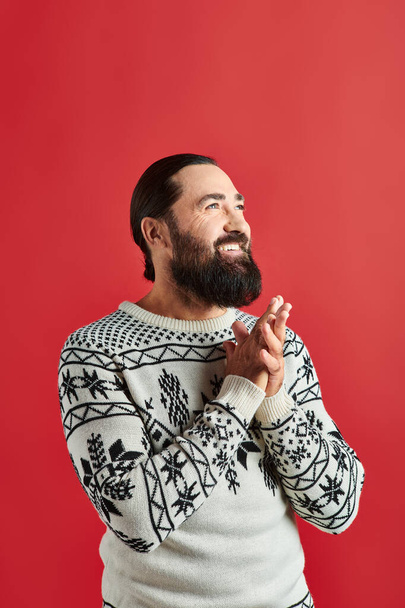 hombre barbudo feliz en suéter de invierno con adorno sonriendo en el telón de fondo rojo, Feliz Navidad - Foto, imagen