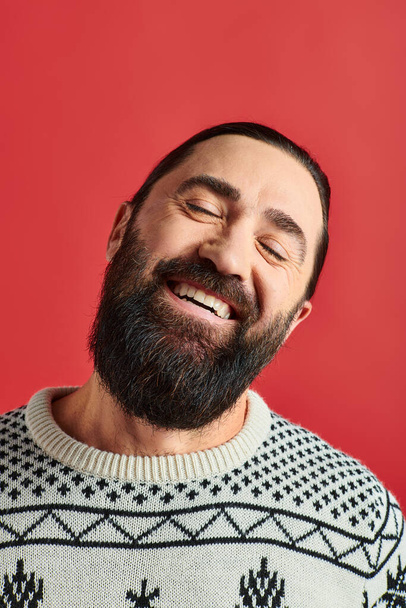 happy bearded man in winter sweater with ornament smiling on red backdrop, Merry Christmas - Photo, Image