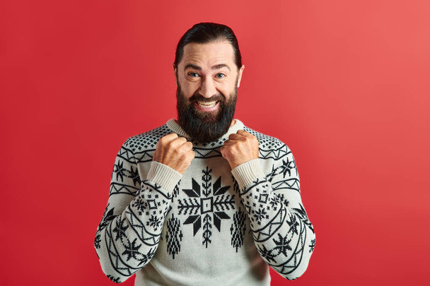 excited  bearded man in winter sweater with ornament smiling on red backdrop, Merry Christmas - Photo, Image
