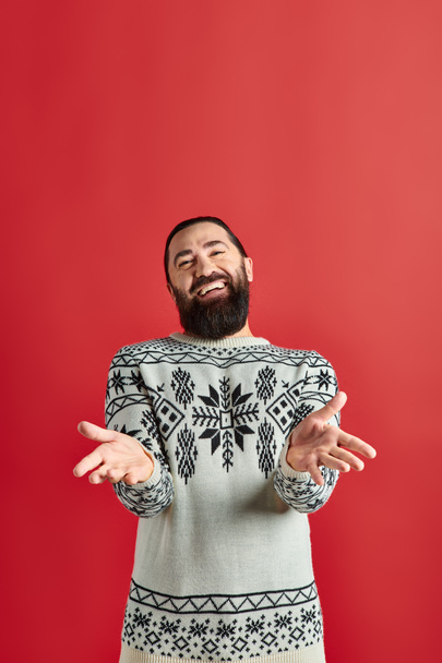 happy bearded man in winter sweater with ornament gesturing on red backdrop, Merry Christmas - Photo, Image