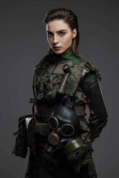 Уверенная женщина-солдат в военной одежде позирует на сером фоне, представляя ближневосточный конфликт - Фото, изображение