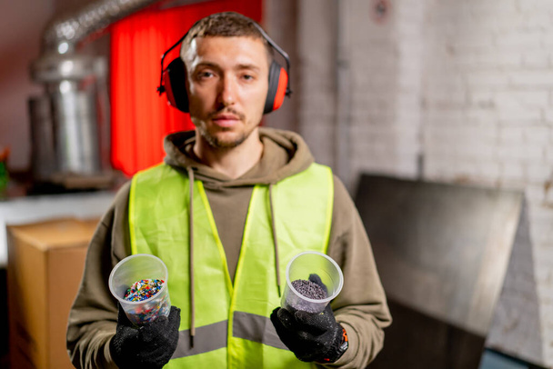 Retrato de um homem de uniforme e fones de ouvido segurando óculos com tampas de plástico trituradas para reciclagem - Foto, Imagem