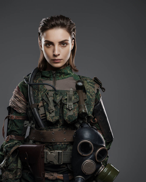 Soldato donna fiduciosa in abiti militari posa su uno sfondo grigio, che rappresenta il conflitto in Medio Oriente - Foto, immagini