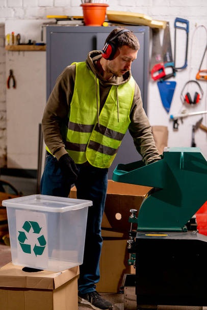Ein Mitarbeiter einer Recyclingstation mit lärmintensiven Kopfhörern schaltet eine spezielle Maschine zum Schreddern gebrauchter Plastikkappen ein - Foto, Bild