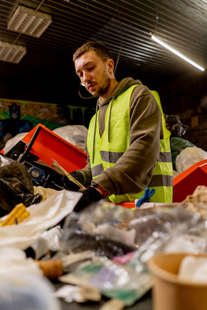An employee in a uniform and gloves at a waste recycling station sorts and sorts garbage on a sorting line - Foto, imagen