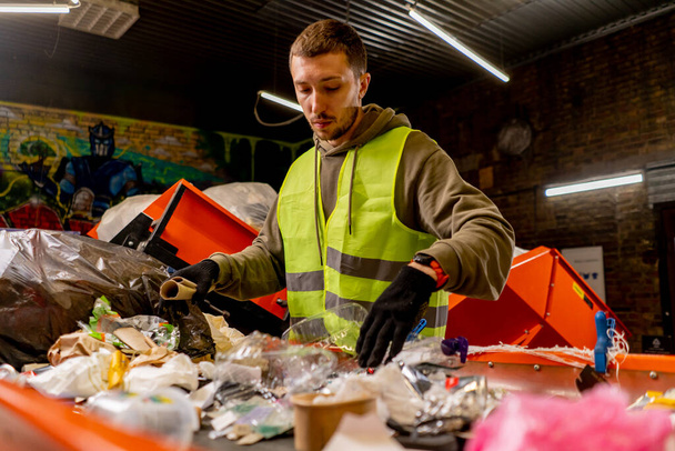 An employee in a uniform and gloves at a waste recycling station sorts and sorts garbage on a sorting line - Foto, Imagem