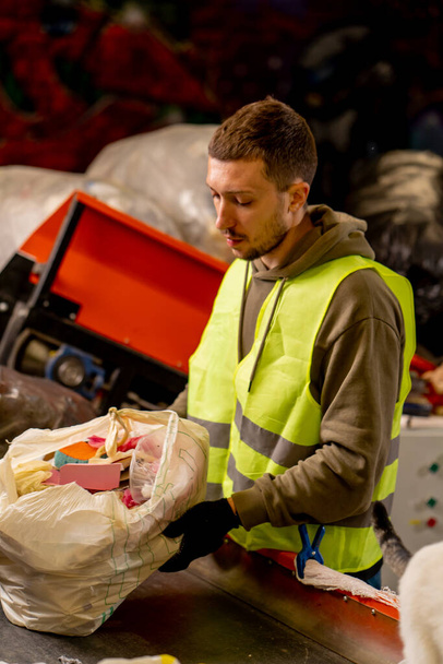 Vista lateral de un hombre de uniforme que trabaja en una línea de distribución de basura y clasifica los residuos en contenedores especiales - Foto, Imagen